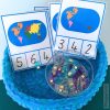 Montessori continent counting cards featuring a colorful world map and numbers for kids to clip the correct answer. Includes a blue basket with colorful clips. Ideal for teaching early counting and geography skills. Designed by happymonti.